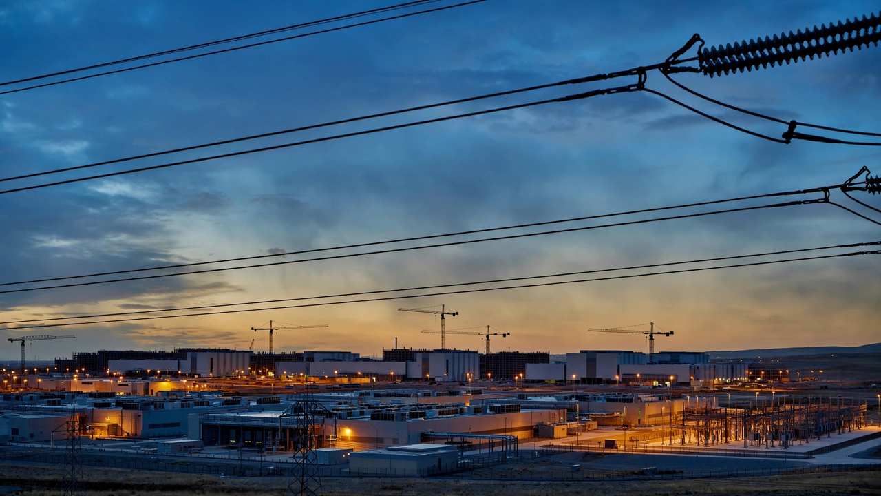 A data center campus at dusk with construction cranes silhouetted.