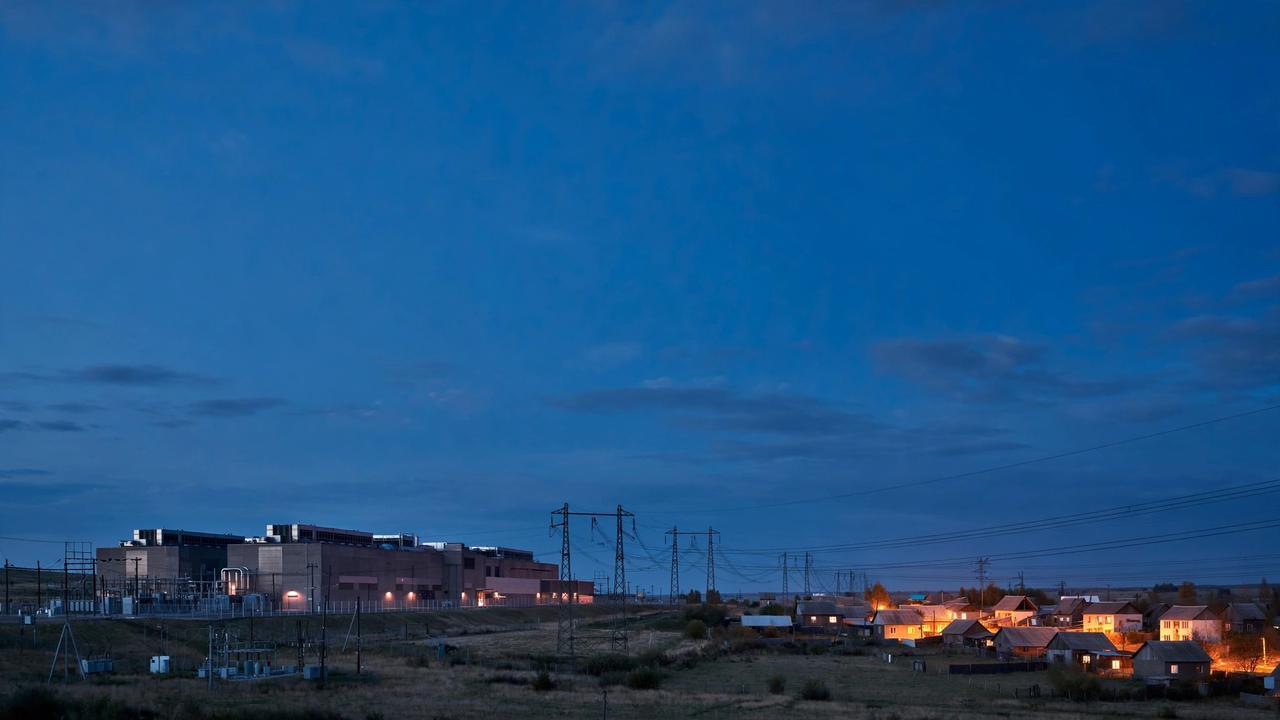 A data center beside a small town at dusk, with power lines running to the houses.