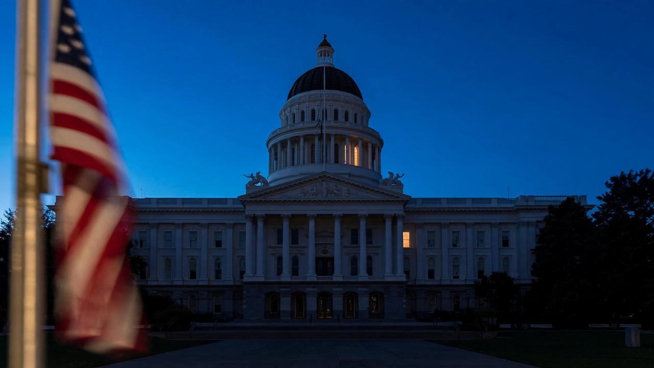 The California State Capitol dome at dusk with one lit window, an empty plaza in front.